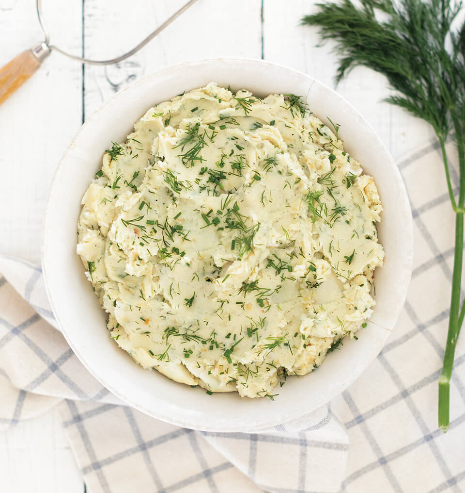 A white bowl of mashed potatoes with dill