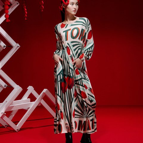 A model in a flowy dress poses in front of a red backdrop