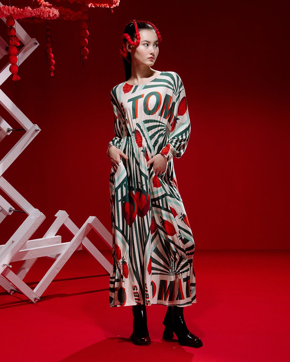 A model in a flowy dress poses in front of a red backdrop