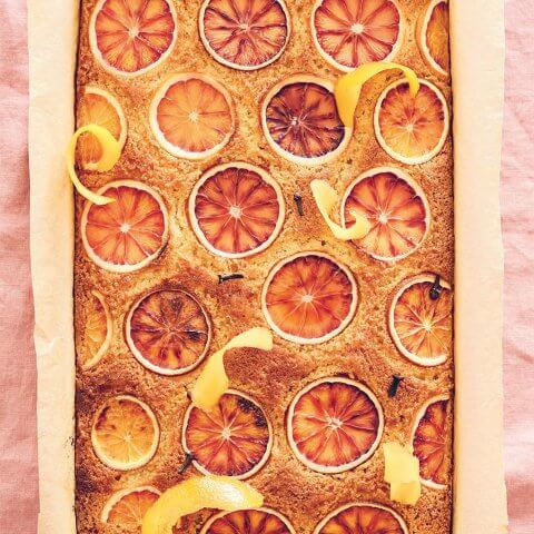 A semolina cake with citrus slices on top over a light pink bagkround