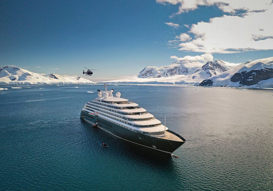 A cruise ship with a helicopter flying behind it in an Arctic peninsula