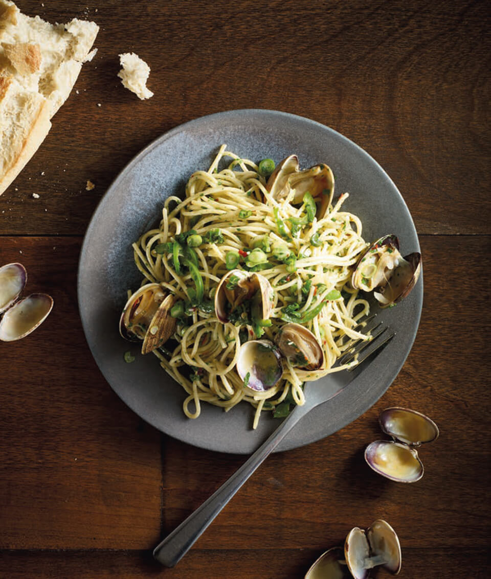 A dish of spaghetti with clams and a piece of bread on a dark wooden surface