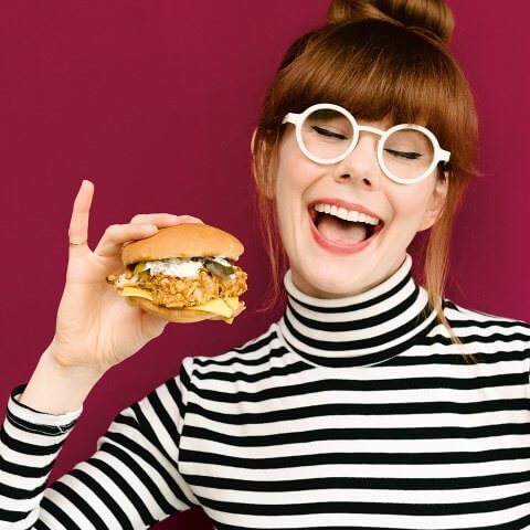 A woman, Mary Berg, holds a fried fish sandwich in front of a red background