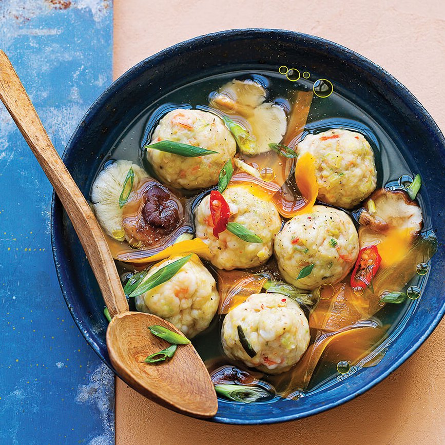 A blue bowl with Thai meatball soup and a wooden spoon.