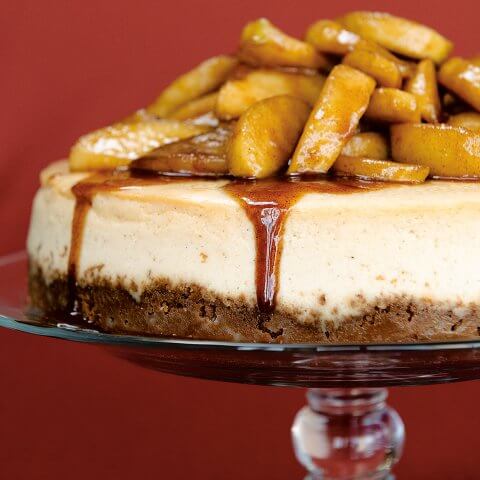 A cheesecake topped with apples against a burgundy wall