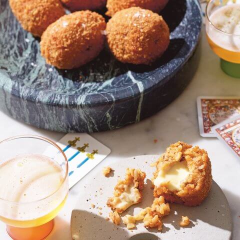 A table with playing cards, cocktails and a marble dish laid with rice balls