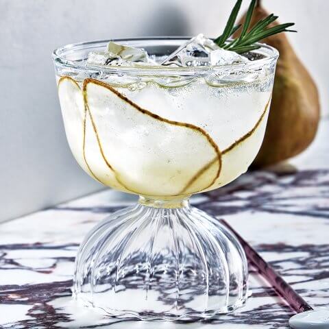 A glass with a drink on a marble surface and a pear visible in the background