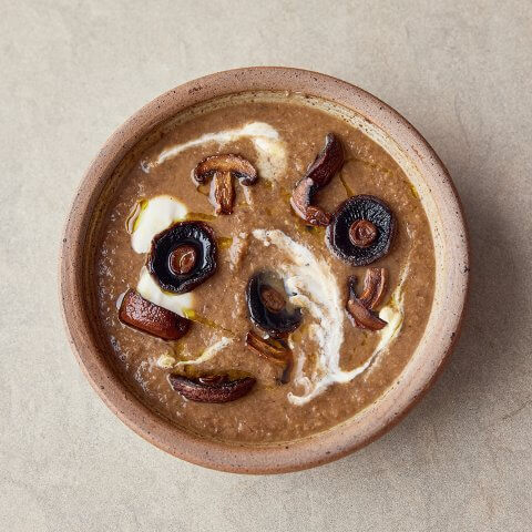 A brown bowl with mushroom soup on a light stone surface