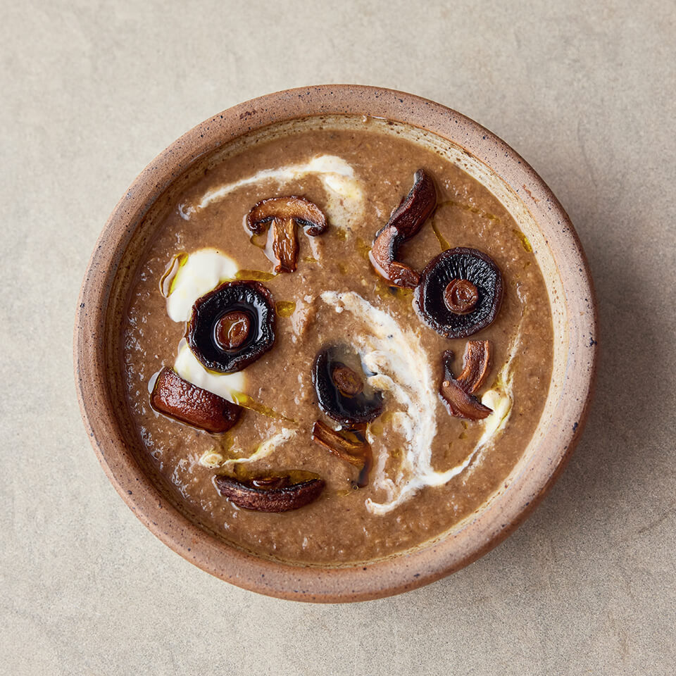 A brown bowl with mushroom soup on a light stone surface