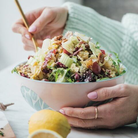 A woman in a turquoise sweater eating from a bowl of salad