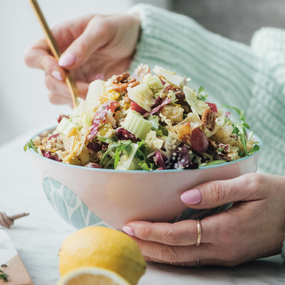 A woman in a turquoise sweater eating from a bowl of salad