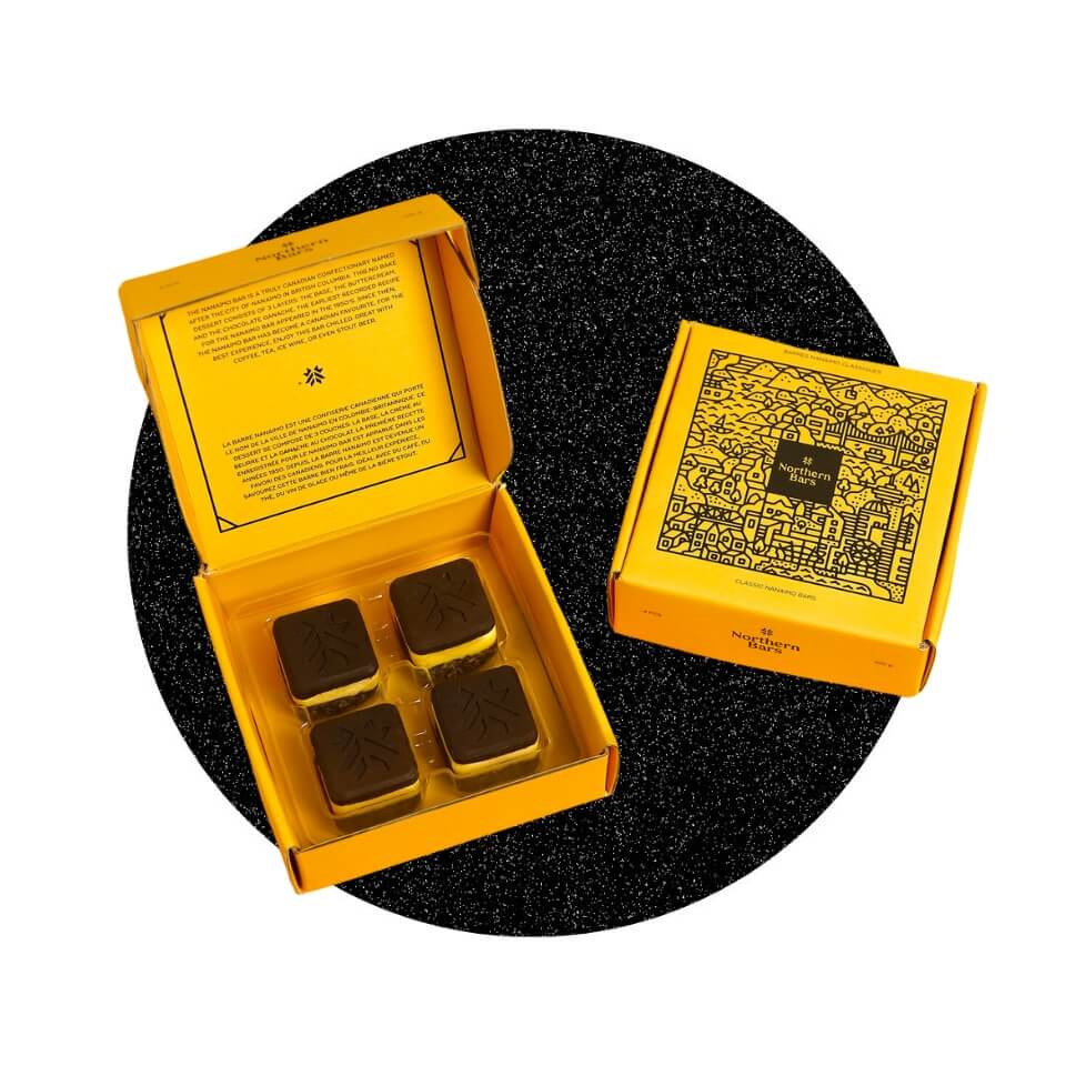 A bright yellow box with four Nanaimo bars and a closed one with a city illustration over a sparkly black circle