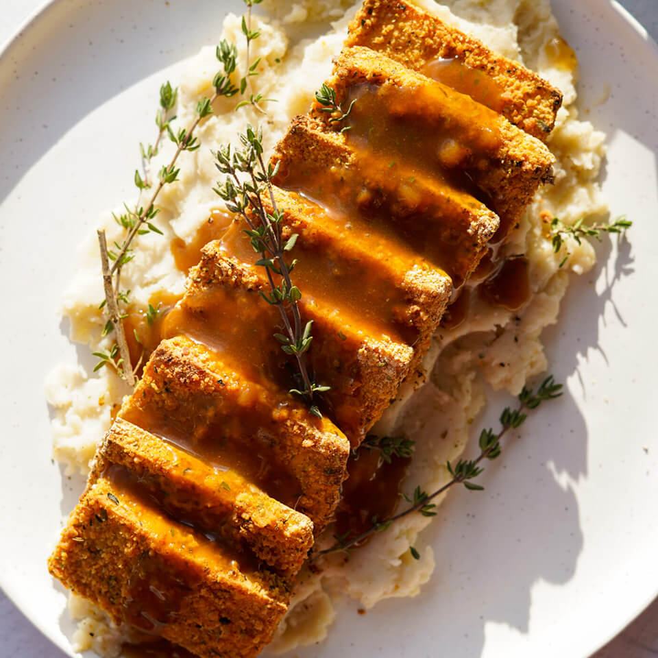 A white plate with crusted tofu pieces over mashed potatoes