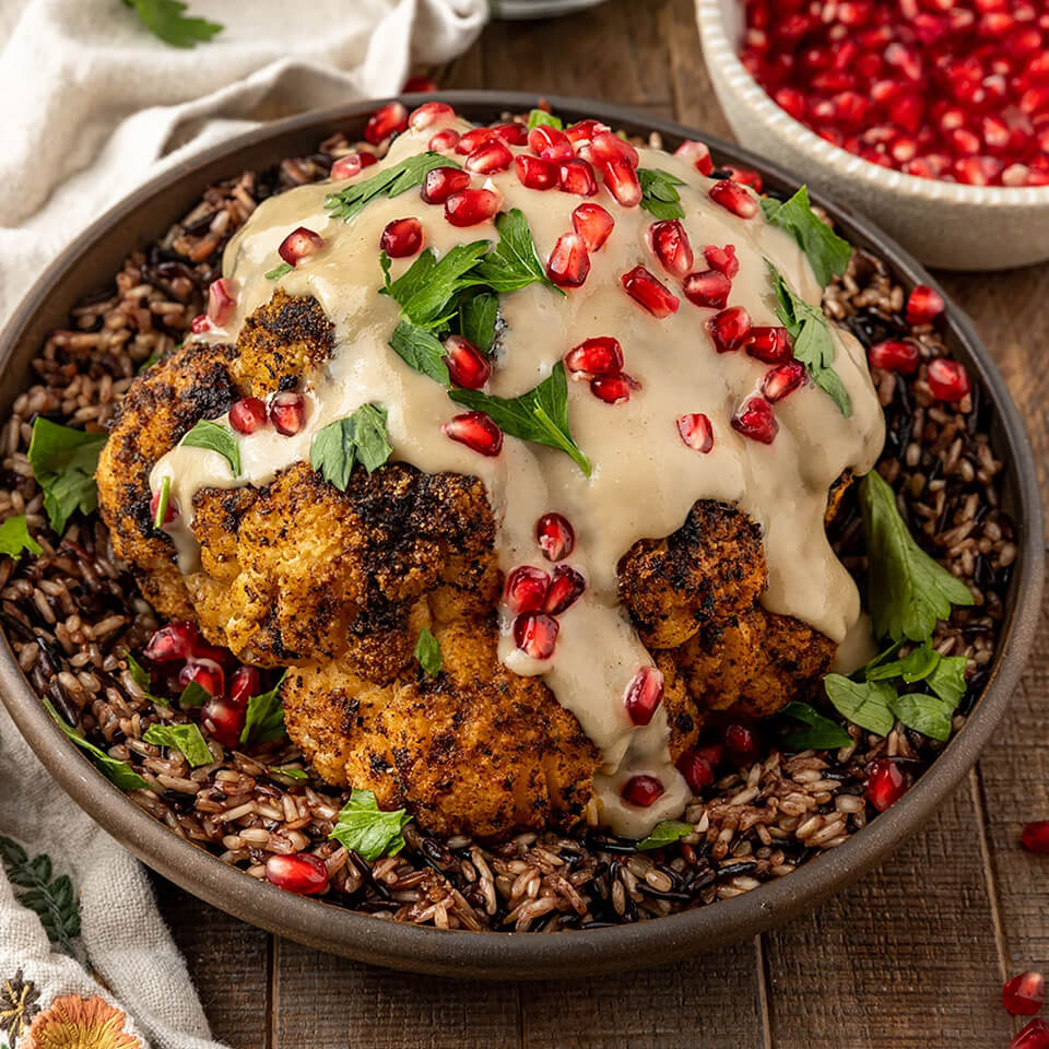 A dish of roasted cauliflower sprinkled with green herbs and pomegranate seeds