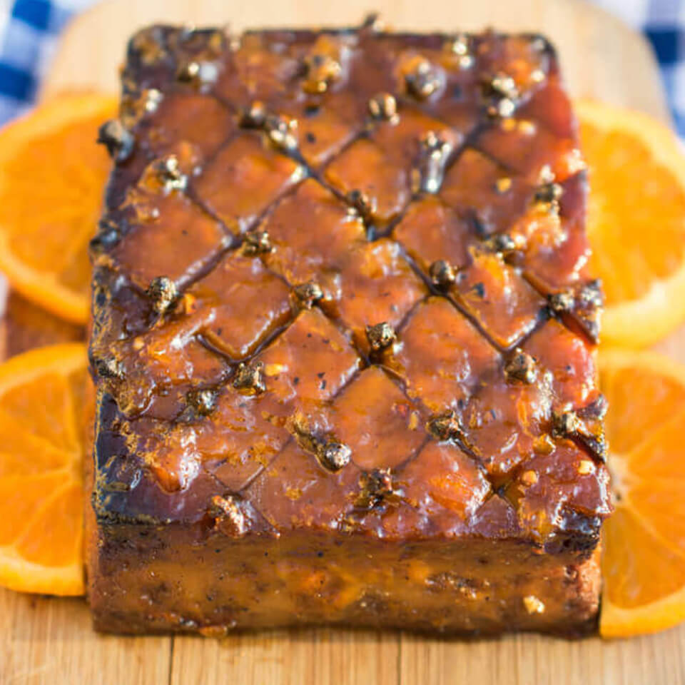 A glazed tofu roast on a wooden cutting board with sliced orange pieces