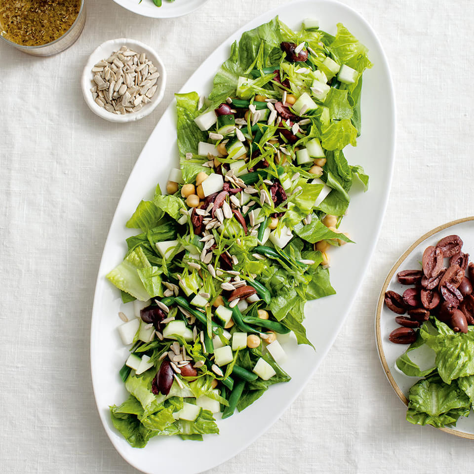 A white platter with salad on a white tablecloth