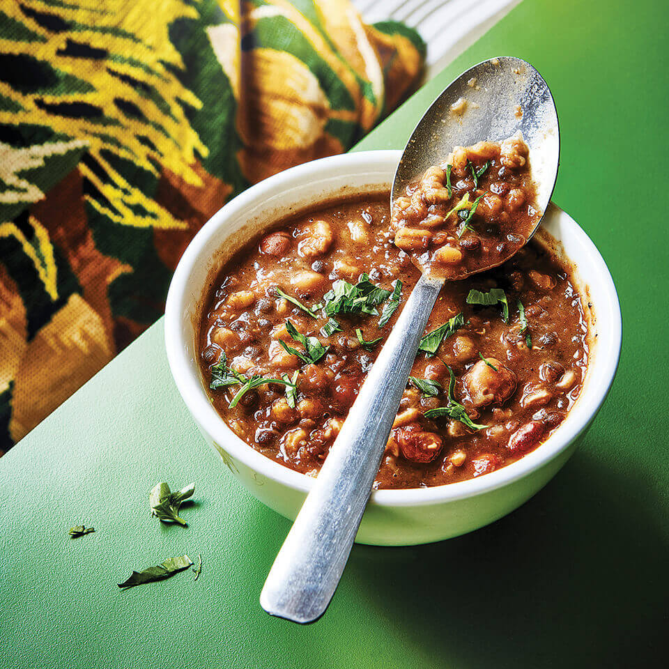 A bowl of lentil stew with a spoon resting over in on a green surface