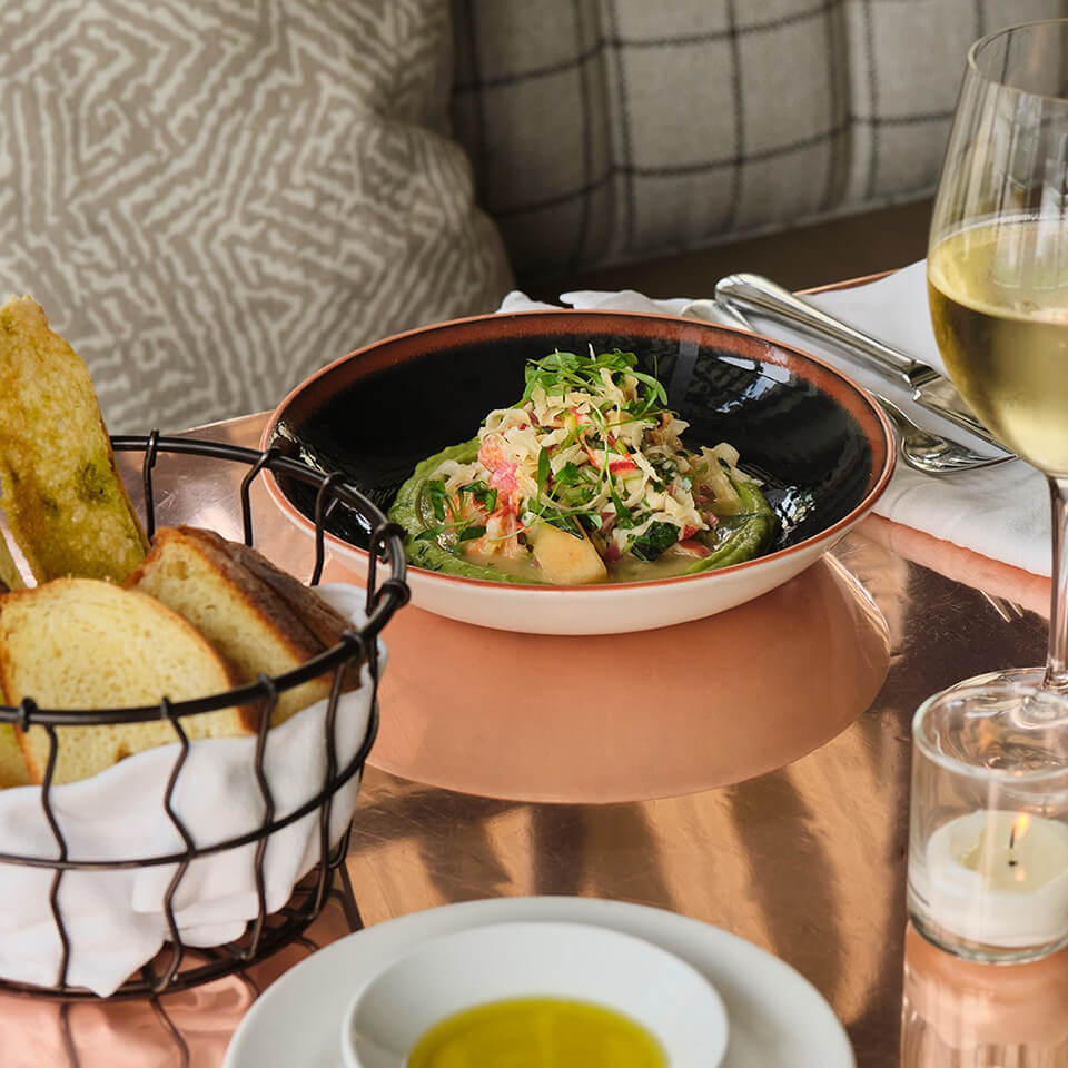 A dish of lobster ceviche and a glass of white wine, with bread and oil on a dining table