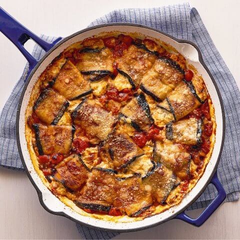 A blue skillet with eggplant and tomato sauce resting on a blue tea towel