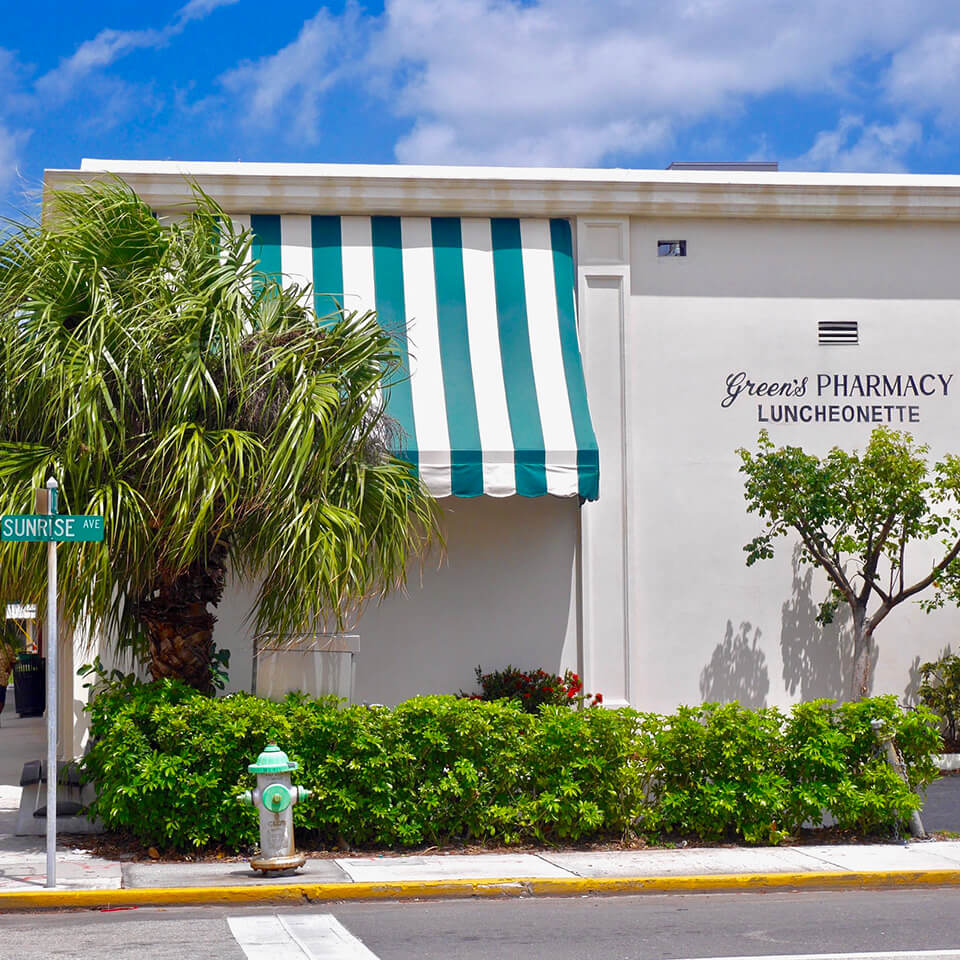 The exterior of a building, Green's Pharmacy Luncheonette, Palm Beach, with palm trees