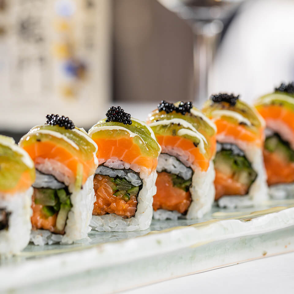A closeup photo of Capt'n Jose spicy salmon sushi roll, with spicy salmon, cucumber, kiwi, black tobiko and a sesame aji mirin aiol