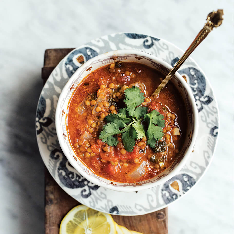 A bowl of lentil soup on a wooden board with lemon wheels