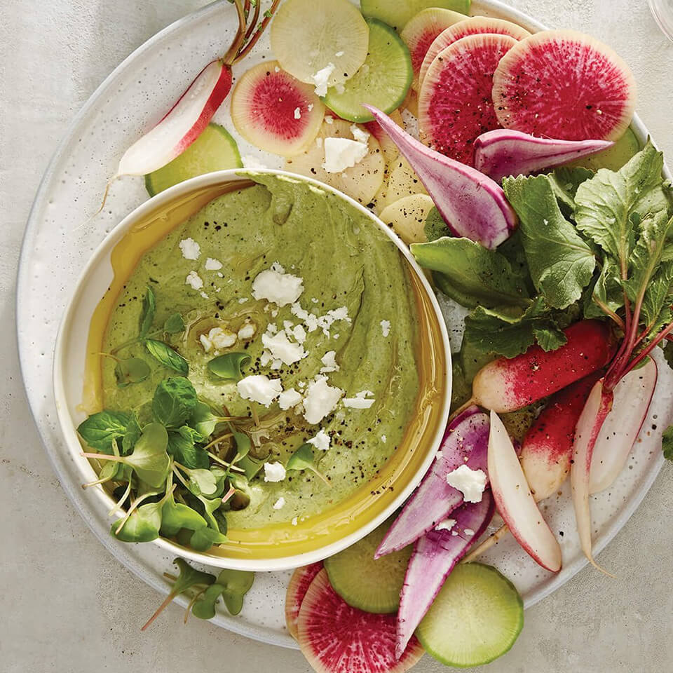 A white dish with vegetables and green dip