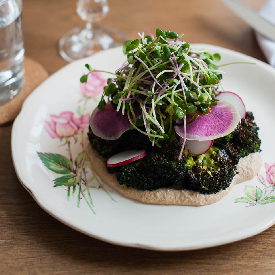A white dish with roasted brassica topped with sprouts