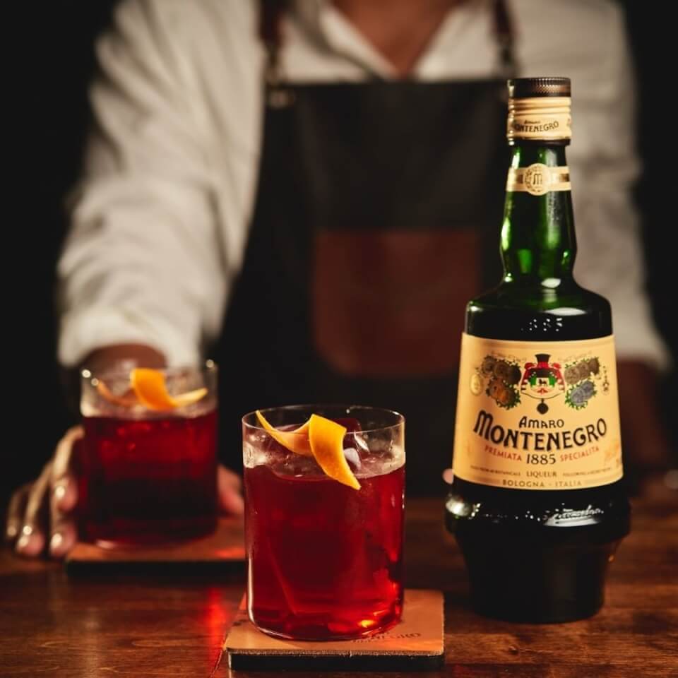 cocktail and bottle of liqueur on bar with man standing behind bar