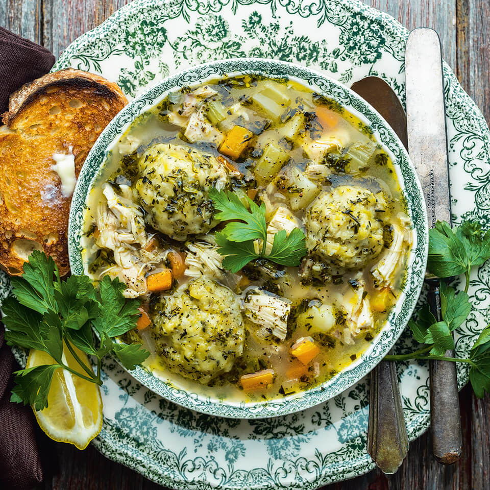 A bowl with chicken stew on a plate with cutlery and a piece of toasted bread