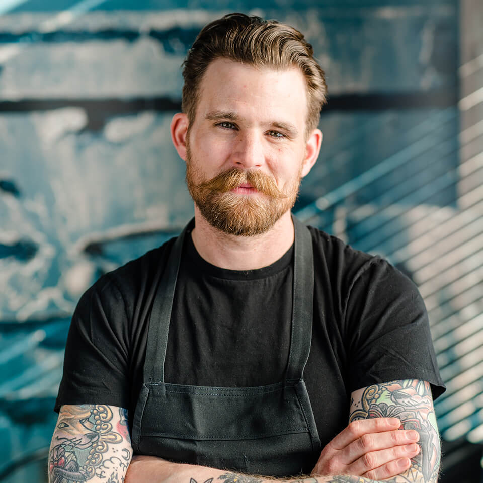 A man, Dale MacKay, smiles while crossing his arms
