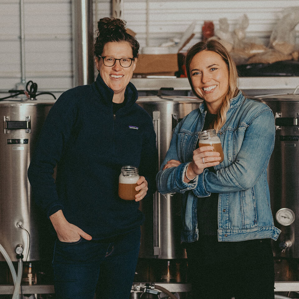 Two women standing in front of stills in a brewery