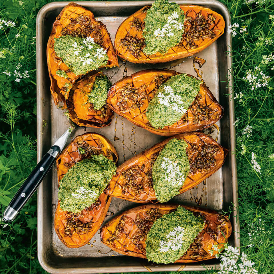 A tray with sweet potatoes topped with pesto resting on green plabts