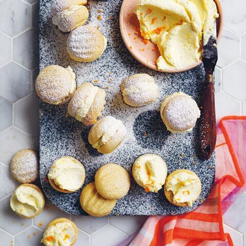 A blue board with a dish of icing and small sandwich cookies