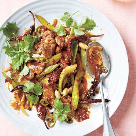 A white plate with lamb stir-fry on a light pink surface