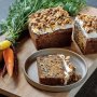 A wooden cutting board with a bushel of carrots Moist vegan carrot cake loaf with cream cheese frosting and walnuts