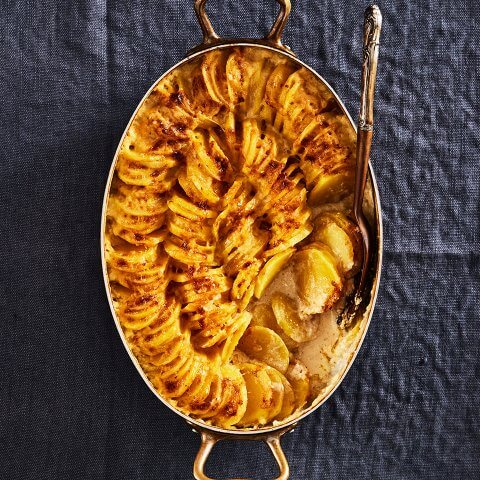 A silver dish of scalloped potatoes topped with cheese on a blue tablecloth