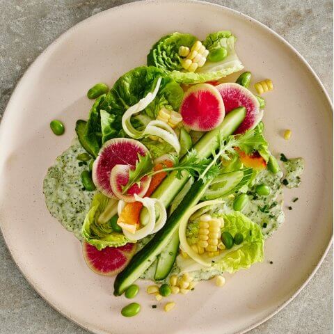 A light pink plate with salad and green goddess salad dressing