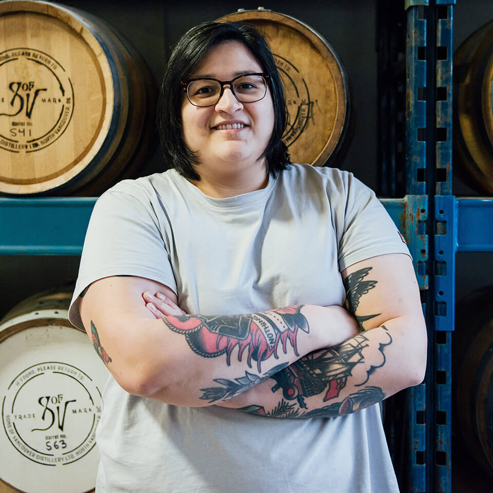 A woman, Jenna Diubaldo, smiles in front of wooden casks