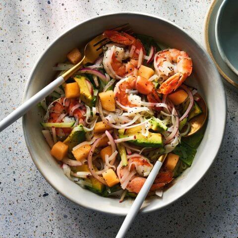 A bowl with salad and a fork and knife photographed from above