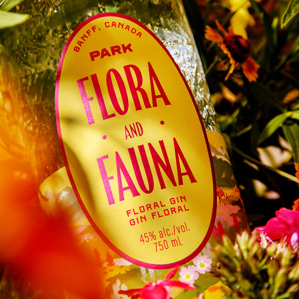 A bottle with a yellow-and-pink label nestled among flowers
