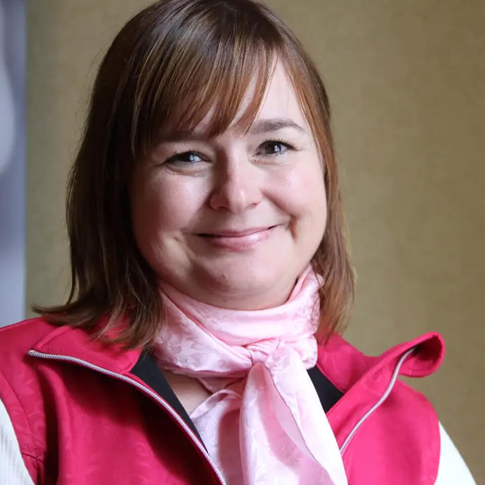 A woman, Susan Echlin, wears a pink vest and scarf and smiles at the camera