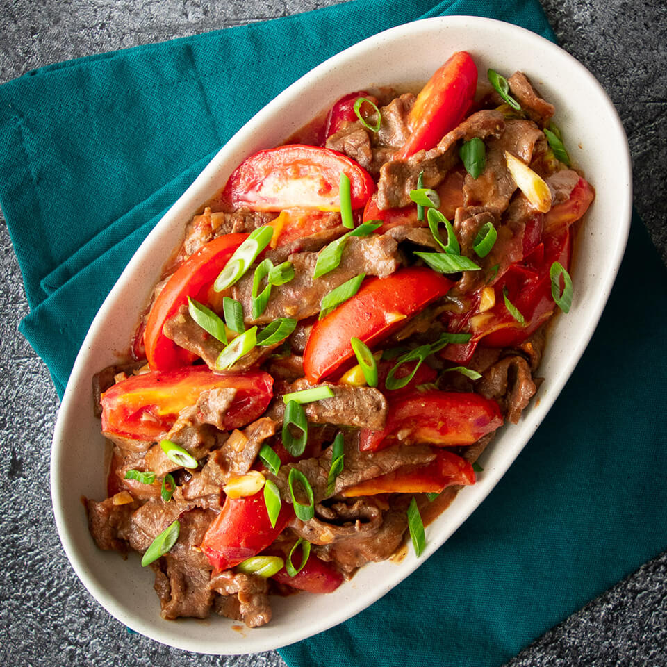 A dish of beef and tomato stir-fry on top of a teal napkin