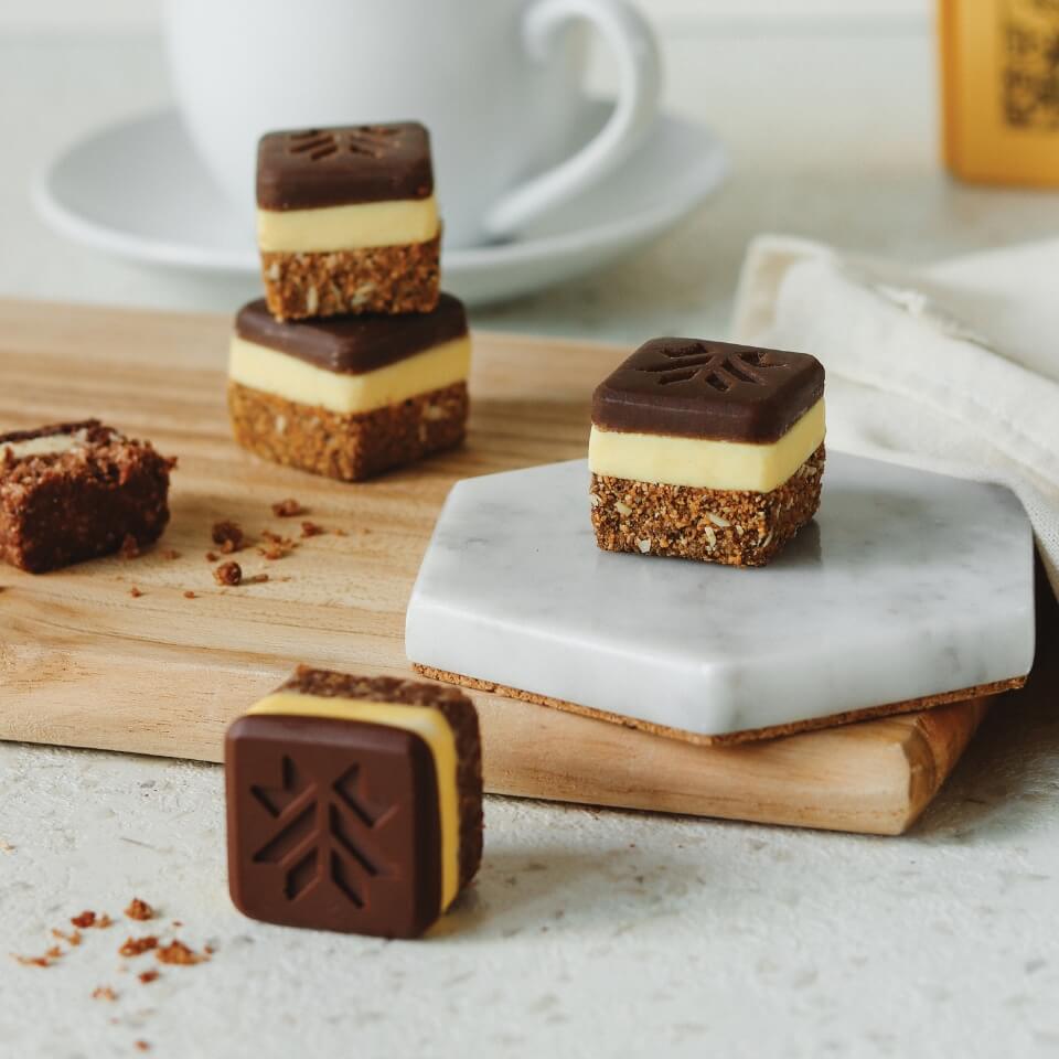 Nanaimo square bars on a wooden board with a mug and yellow box visible behind them