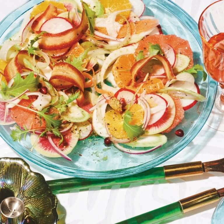 Bright citrus salad with fennel, arugula, radish and herbs on a blue plate.