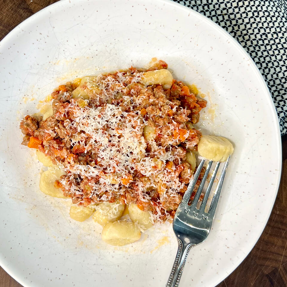 A speckled white dish with gnocchi and bolognese sauce
