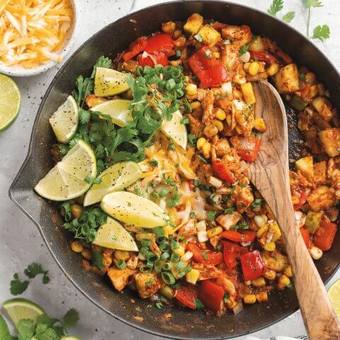 A skillet witch chicken, rice, vegetables and lime wedges