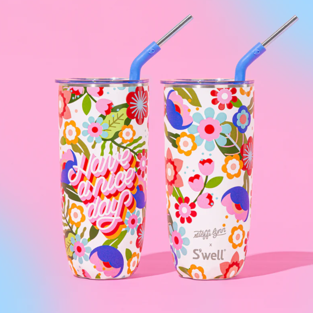 Two colourful floral-patterned tumblers with silver straws in front of a pink and blue ombre background.