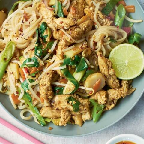 A blue dish with pad thai and chopsticks and a sauce dish visible next to it