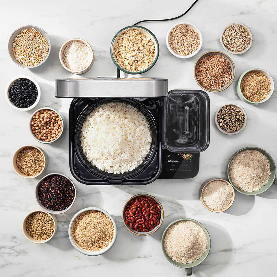A rice cooker surrounded by cups with different varieties of grains